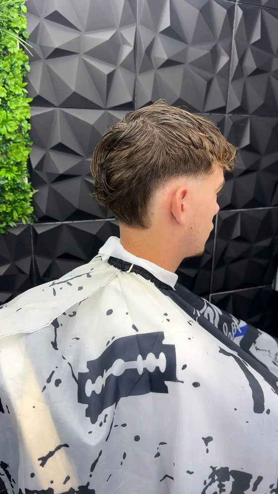 Coupe vue de profil : dégradé bas sur les côtés et longueurs texturées sur le dessus, devant le mur végétal