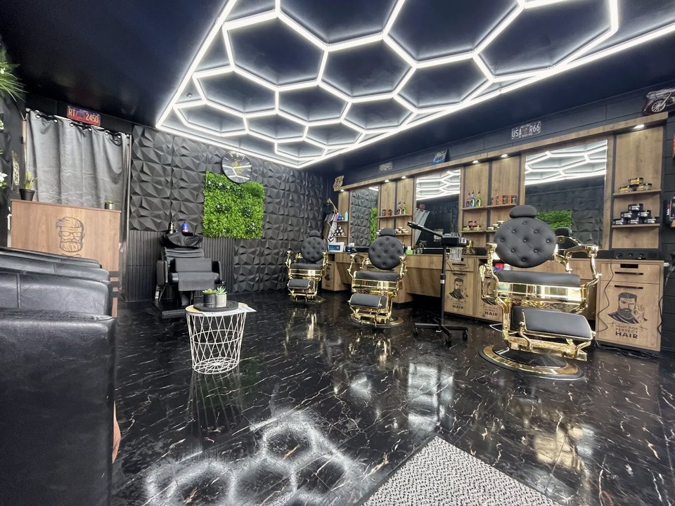 Vue d’ensemble du salon : bac à shampoing, mur végétal, comptoirs en bois et plafond en nid d’abeille lumineux reflété dans les miroirs